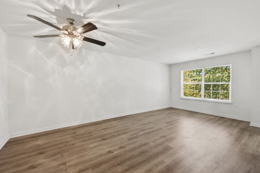 an empty living room with a ceiling fan and a window